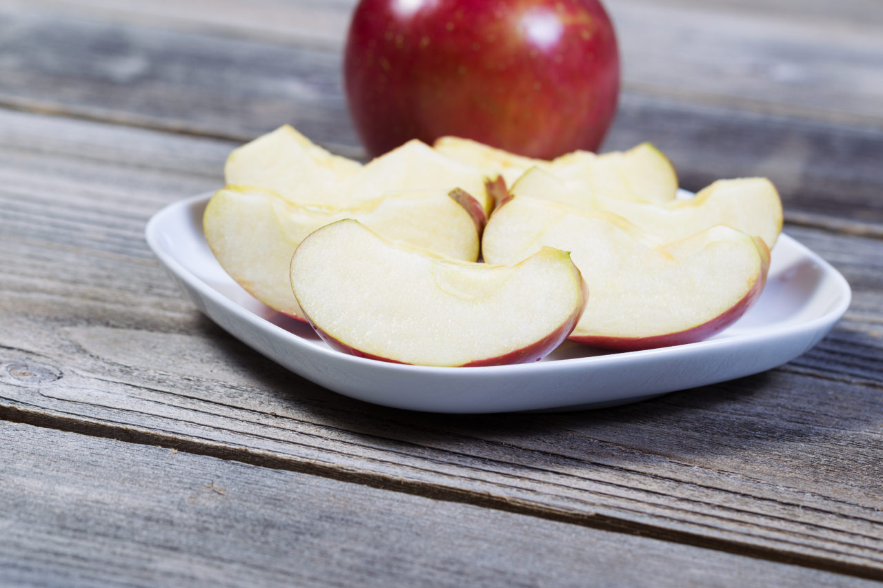 Horizontal photo of fresh apple slices, on white plate, with whole apple and rustic wood in background
